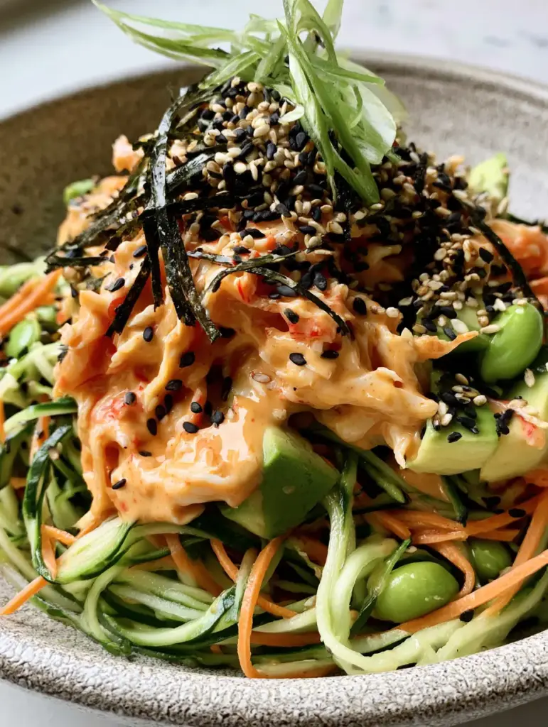 California Roll Cucumber Salad: The Ultimate Deconstructed Sushi Bowl 2 A close-up, handheld smartphone photo of a california roll cucumber salad featuring glossy pale orange sriracha mayo and bright green edamame.